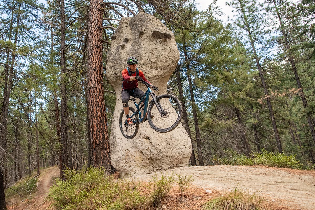 A mountain biker takes a big jump in front of a rock.